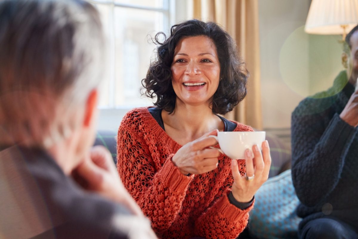 A woman talking to a man while drinking tea.