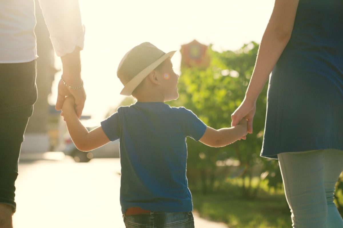 A family with a young child holding hands outdoors.